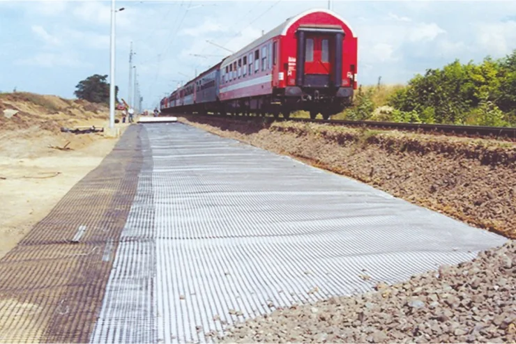 Geocomposite reinforcement installed along a railway track to stabilize the ground, with a red train moving in the background.