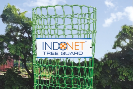 Green plastic square tree guard with "Indonet Tree Guard" label, placed outdoors among trees for plant protection.